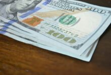 here's a short caption: hundred dollar bills stacked on a table.